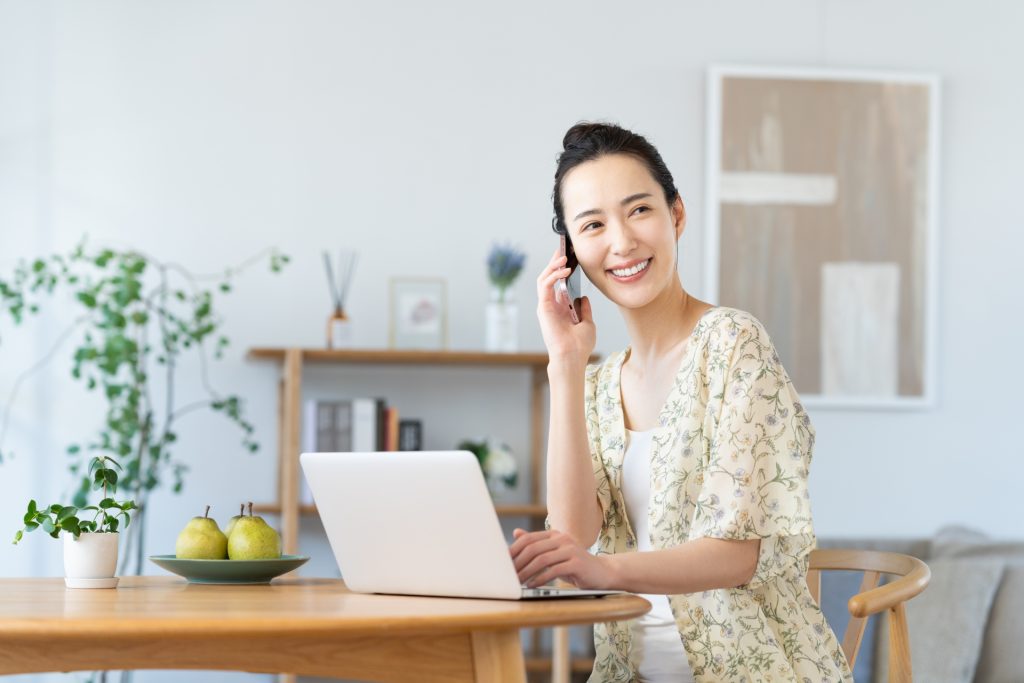 パソコンをしながら電話をする若い女性