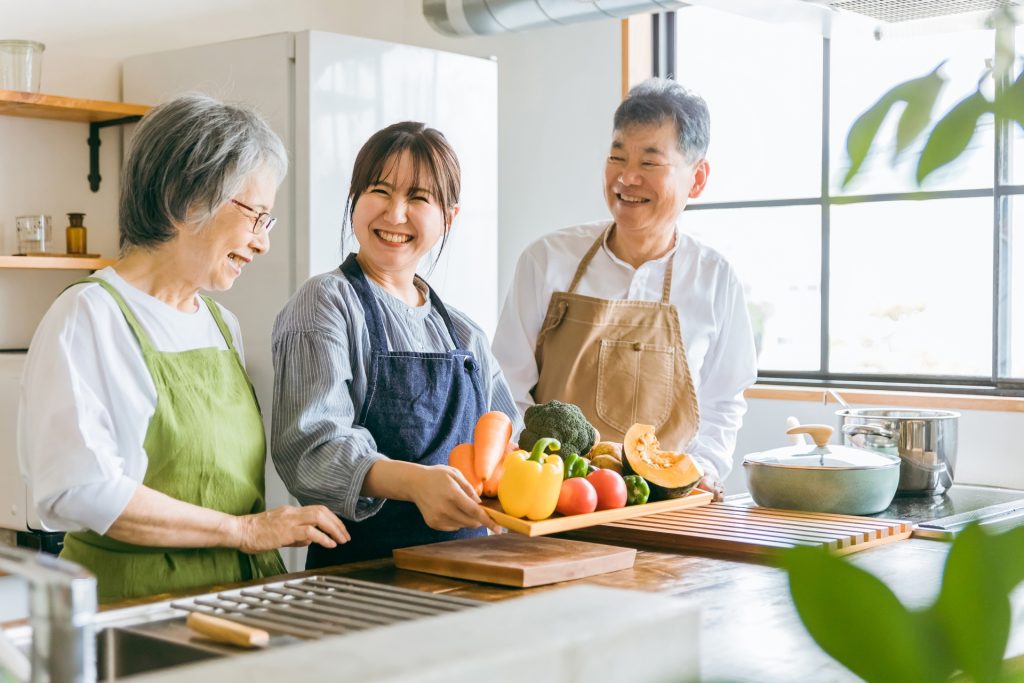 野菜を持つ高齢者夫婦と若い女性（介護）