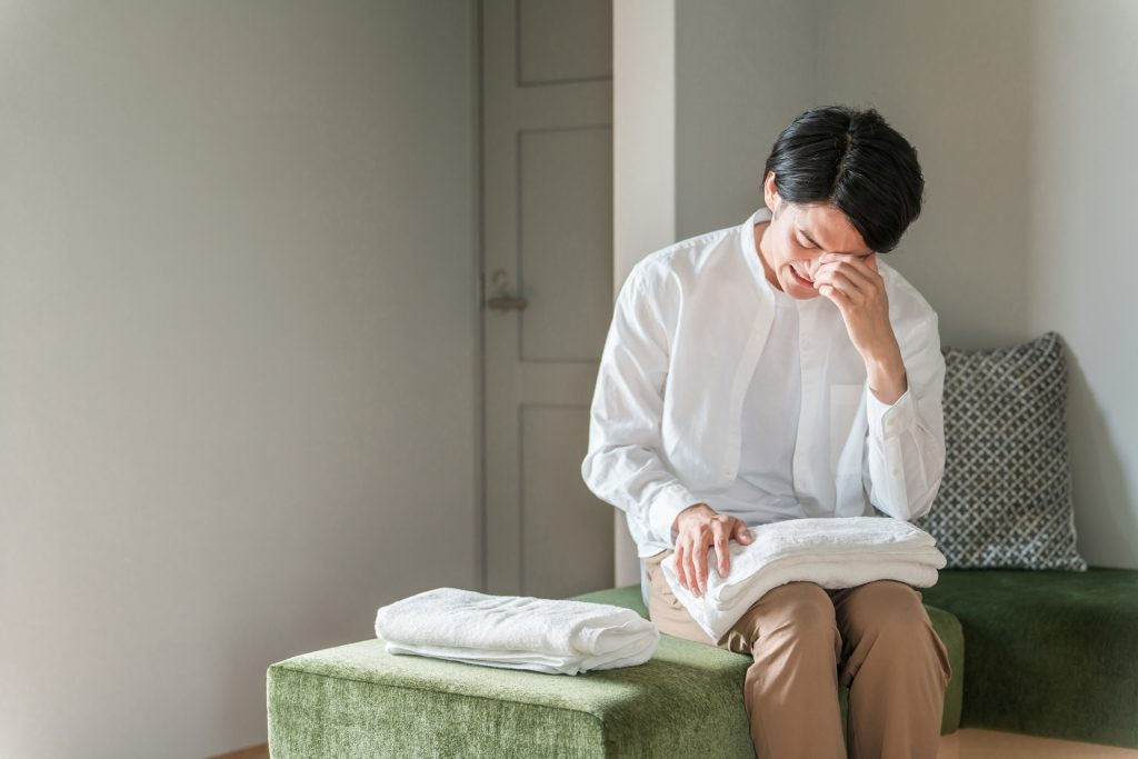 自宅で洗濯物を畳みながら泣く男性(離婚)