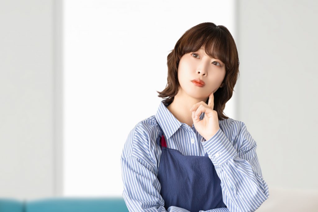 考えごとをするエプロン姿の女性