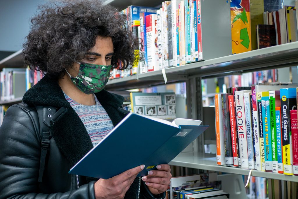 本棚の前で本を開いて読む男