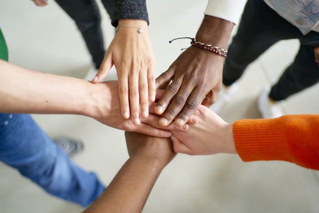 多様な人種や文化を表現する、異なるスキントーンの5本の手が重ねられた団結のシンボル写真