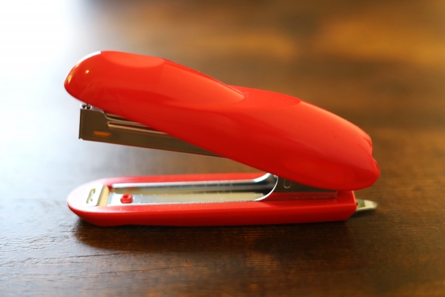 トマトレッドカラーのホッチキス(ステープラー)のクローズアップ画像。自毛植毛手術で使用されるパンチ機器の形状が一般的なホッチキスに似ていることから、その比較対象として用いられるイメージ写真