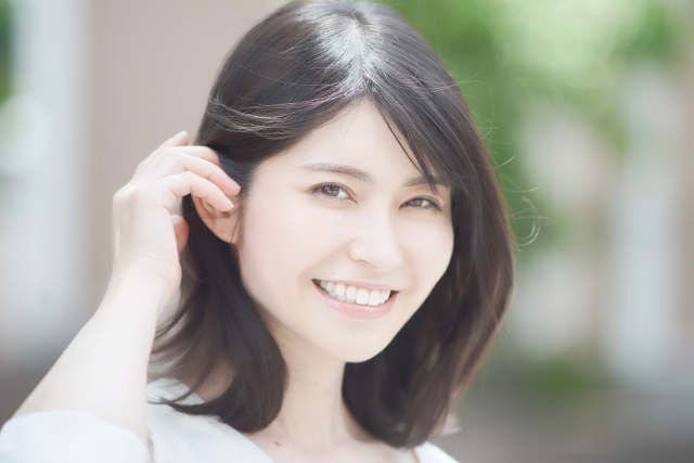 ツヤのある髪を右耳にかけながら微笑む日本人女性|美髪ケア・ヘアスタイルの参考に最適